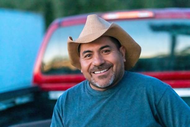 Smiling Hispanic farm worker posing wearing a cowboy hat looking at the camera stock photo