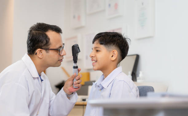 Smiling Indian boy doing eye test checking examination with optometrist in optical store stock photo