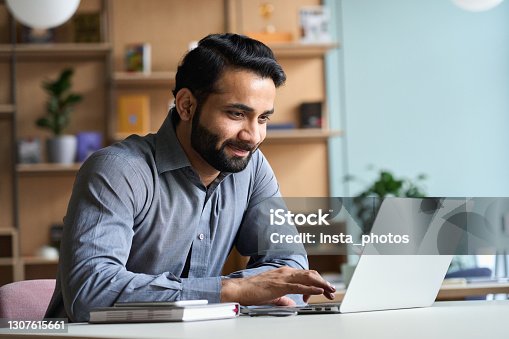 istock Smiling indian business man working on laptop at home office. Young indian student or remote teacher using computer remote studying, virtual training, watching online education webinar at home office. 1307615661