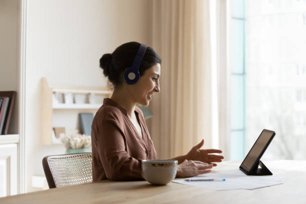 Smiling Indian woman in earphones talk on webcam on pad stock photo