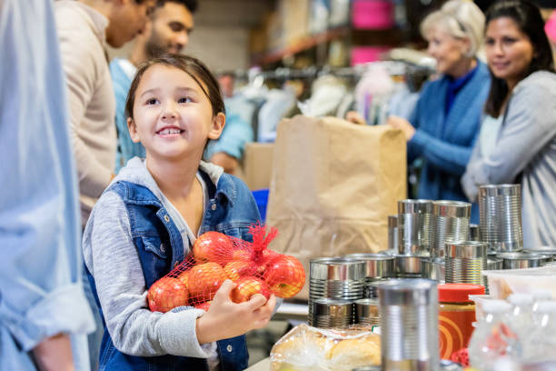 Smiling little girl donates apples to food bank Happy little girl holds a bag of apples while volunteering with her family in a community food bank. food bank stock pictures, royalty-free photos & images
