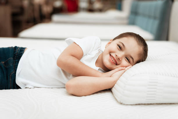 una niña sonriente yace en un colchón ortopédico en una tienda de muebles. - mattresses for children  fotografías e imágenes de stock