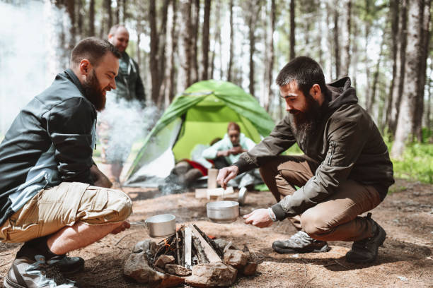 lächelnde männliche camper machen eintopf für ganzes camp - fett verbrennen senior stock-fotos und bilder