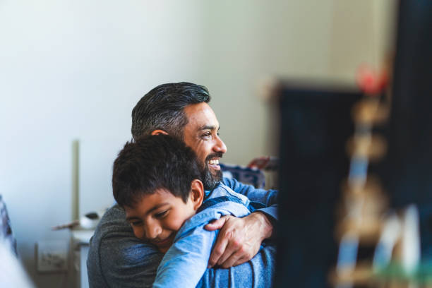Smiling man embracing son in bedroom at home Smiling man embracing boy in bedroom. Happy father is looking away with son at home. They are spending leisure time. looking away photos stock pictures, royalty-free photos & images