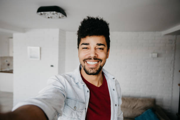 lächelnd mann im wohnzimmer ist eine selfie nehmen. - selfie stock-fotos und bilder