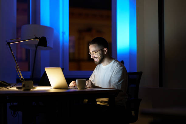 Smiling man talk using online video call in dark office stay overtime to communicate with coworkers stock photo