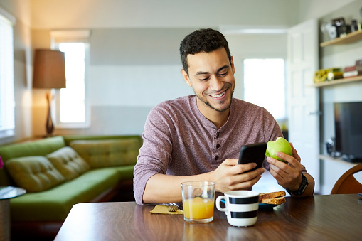 Smiling man using mobile phone while holding apple