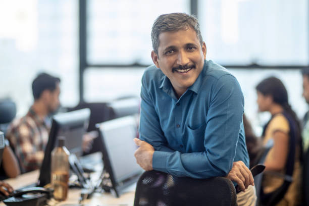 Smiling mature manager sitting at creative office Portrait of smiling mature manager leaning on chair. Confident male entrepreneur is at creative office. He is in formalwear. india stock pictures, royalty-free photos & images