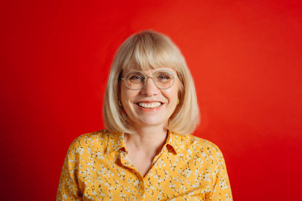 Smiling mature woman in glasses on red background Smiling mature woman in glasses on red background russian mature women stock pictures, royalty-free photos & images