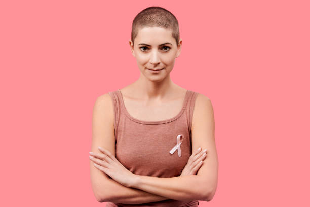 smiling mid 30s woman, a cancer survivor, wearing pink breast cancer awareness ribbon, isolated over living coral background. support, solidarity, screening and prevention concept. - beleza doentes cancro imagens e fotografias de stock