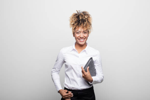 Smiling mid adult businesswoman with office diary Portrait of smiling mid adult businesswoman with office diary. Confident female manager is wearing white shirt. She is having curly hair against white background. secretary stock pictures, royalty-free photos & images
