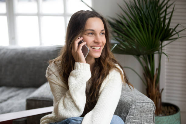 Smiling millennial mestizo woman talking on the phone at home Smiling millennial mestizo woman talking on the phone at home, happy young girl holds cellphone making answering call, attractive teenager having pleasant conversation chatting by mobile with friend big smile emoji stock pictures, royalty-free photos & images