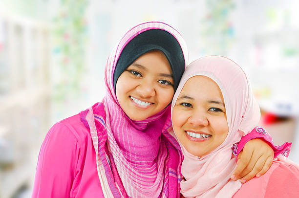 Smiling Muslim women in pink traditional garb Happy Muslim women standing inside house  indonesian woman stock pictures, royalty-free photos & images