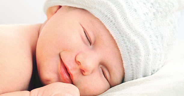 smiling newborn baby in white hat stock photo