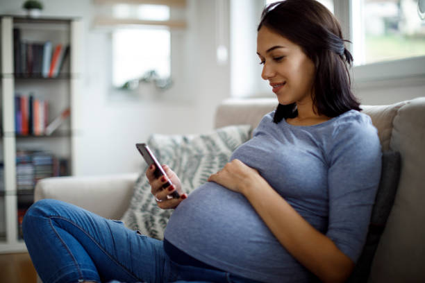 Smiling pregnant woman using mobile phone at home stock photo