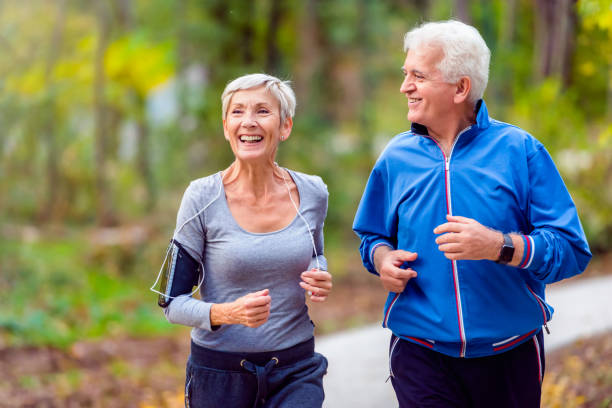 älteres paar im park joggen lächelnd - joggen stock-fotos und bilder