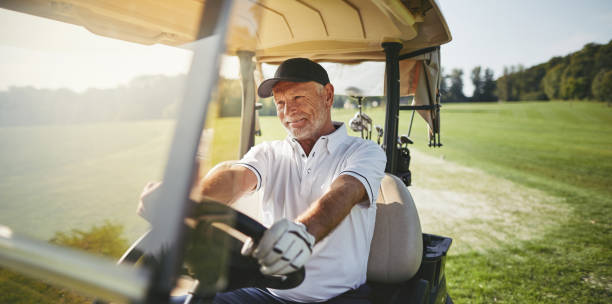 Smiling senior man driving his golf cart on a fairway stock photo