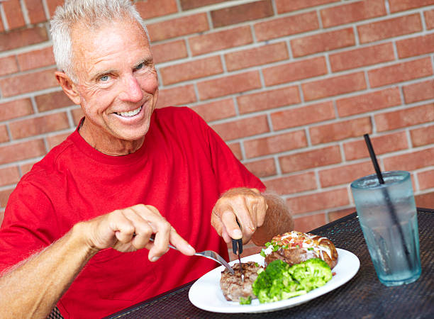 Smiling Senior Man Eating Strip Steak At Restaurant Table stock photo