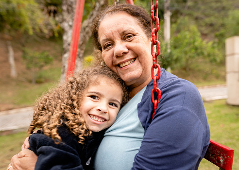 Portrait of a smiling senior woman and her cute little granddaughter sitting together outside on a swing at home