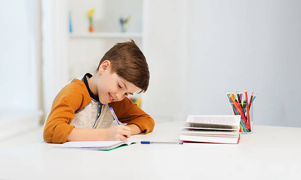 smiling student boy writing to notebook at home - huiswerk stockfoto's en -beelden