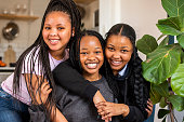 istock Smiling teenage girls sitting arm in arm together at home 1356645587