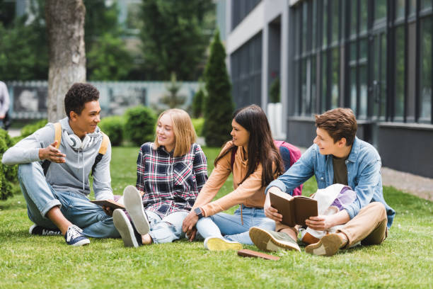 lachende tieners zittend op gras, praten en het houden van boeken - alleen tieners stockfoto's en -beelden