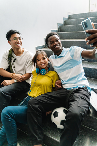Smiling teens Asian and African Smiling young Asian and African teenager student friends taking photo selfie with phone in the stairs of Secondary School