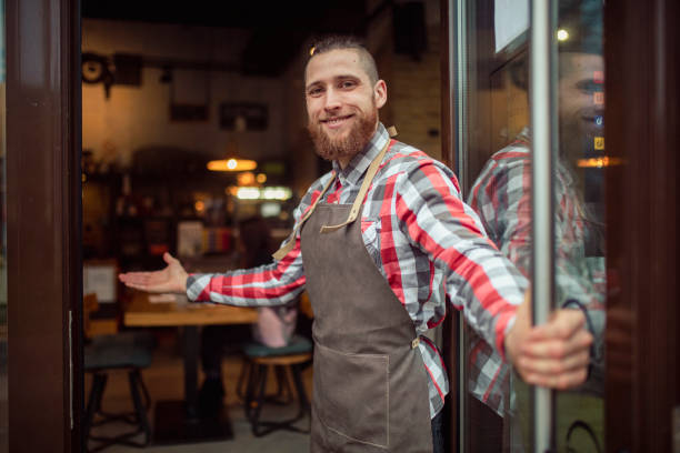 A smiling waiter with an apron greets restaurant guests and welcomes them. stock photo