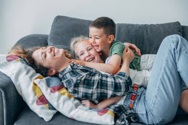Smiling woman and two kids playing in the living room. Happy young mother playing on the sofa with her cute son and daughter. tickling beautiful women pictures stock pictures, royalty-free photos & images