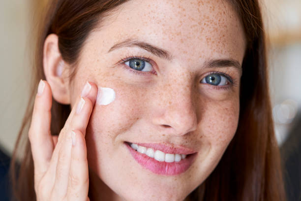 Smiling woman applying cream on her face Portrait of smiling young woman with freckles applying cream on her face applying face cream stock pictures, royalty-free photos & images