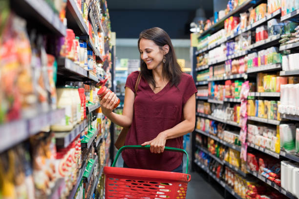 Smiling woman at supermarket Happy mature woman looking at product at grocery store. Smiling hispanic woman shopping in supermarket and reading product information. Costumer buying food at the market. groceries stock pictures, royalty-free photos & images