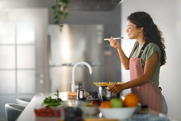 smiling woman enjoying while cooking spaghetti for lunch. - keuken stockfoto's en -beelden