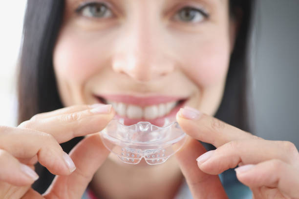Smiling woman holds clear plastic mouthguard to straighten teeth stock photo