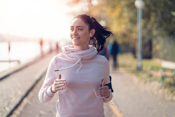 Smiling woman jogging and listening to music Young attractive woman listening to music while jogging on the park alleys Portable DVD Player stock pictures, royalty-free photos & images