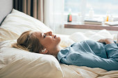 Happy blonde woman in blue pajamas lying in bed in the morning and listening to relaxing music.