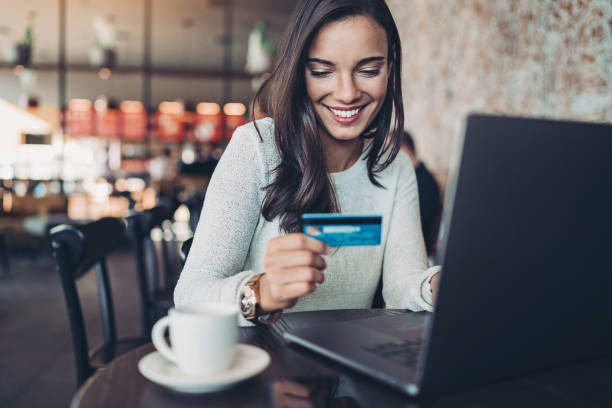 Smiling woman making a credit card purchase Smiling businesswoman holding a credit card and using laptop in a restaurant credit card purchase stock pictures, royalty-free photos & images