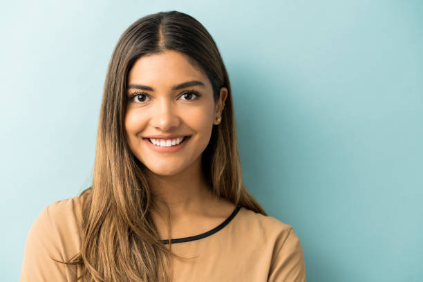 Smiling Woman Standing Against Blue Background Happy young Hispanic woman with long hair in studio mexican woman stock pictures, royalty-free photos & images
