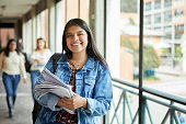 Portrait of smiling young woman standing in corridor. Female student is standing by window in university. She is in casual.