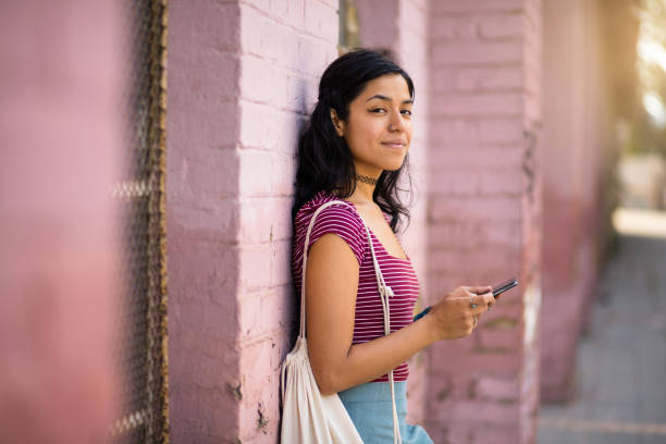 Smiling woman standing on street and holding phone. stock photo