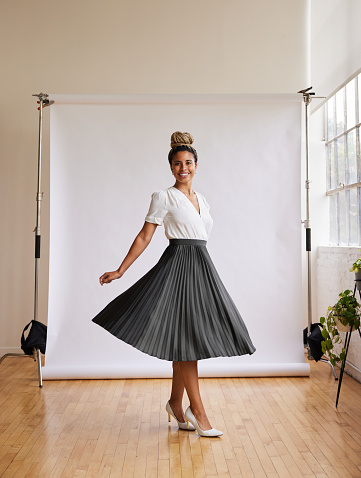Portrait of a smiling young African American woman twirling a long skirt in front of a white backdrop