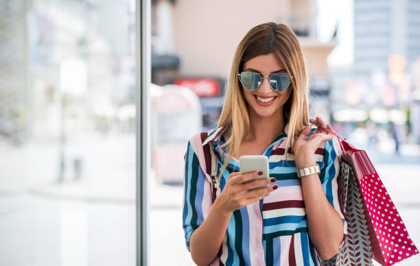 Smiling woman using mobile phone during the shopping in the city. Consumerism, lifestyle concept stock photo