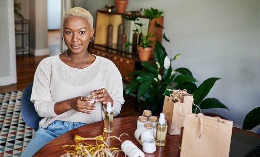 Portrait of a smiling young African female influencer sitting at a table and preparing products for a vlog post