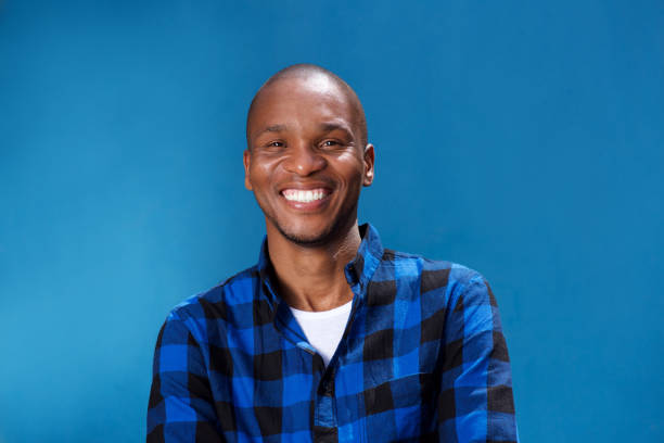 smiling young african man smiling against blue wall stock photo