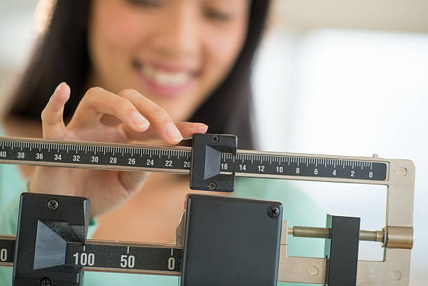 Smiling young Asian woman adjusting a weight scale stock photo