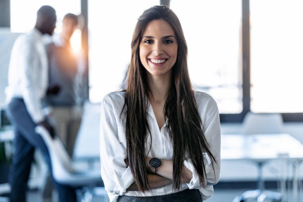 lächelnde junge geschäftsfrau, die in die kamera schaut, während sie im coworking space steht. - business woman stock-fotos und bilder