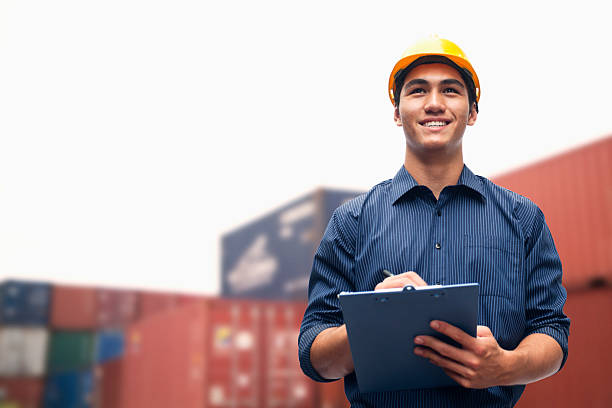 Smiling young engineer in a shipping yard examining cargo stock photo