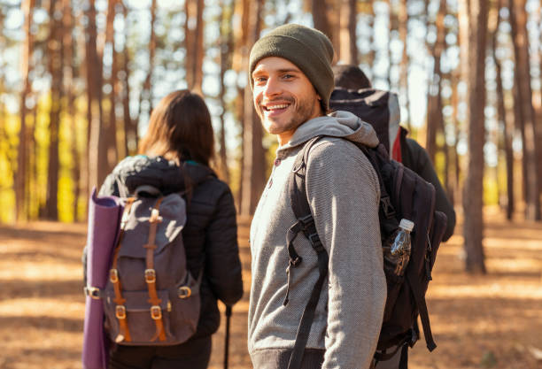 glimlachende jonge mensen backpacker die met vrienden bij bos wandelt - klimbos stockfoto's en -beelden
