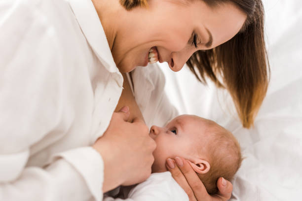 sorridente giovane madre in t-shirt bianca che allatta il bambino - allattamento foto e immagini stock