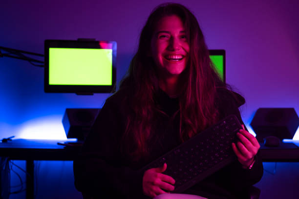 Smiling young woman holding keyboard in front of her computer desk stock photo
