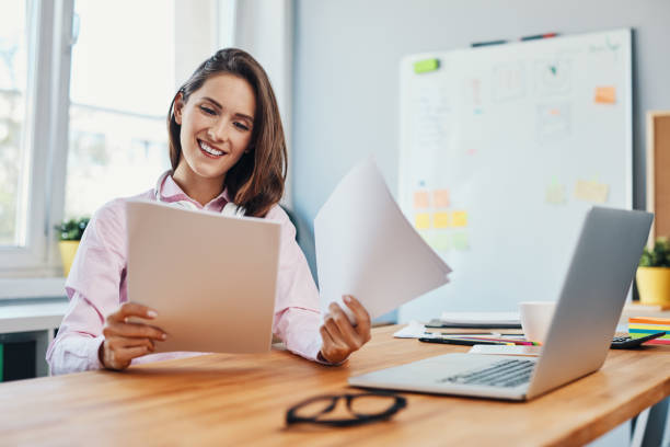 Smiling young woman looking at business documents working in home office stock photo